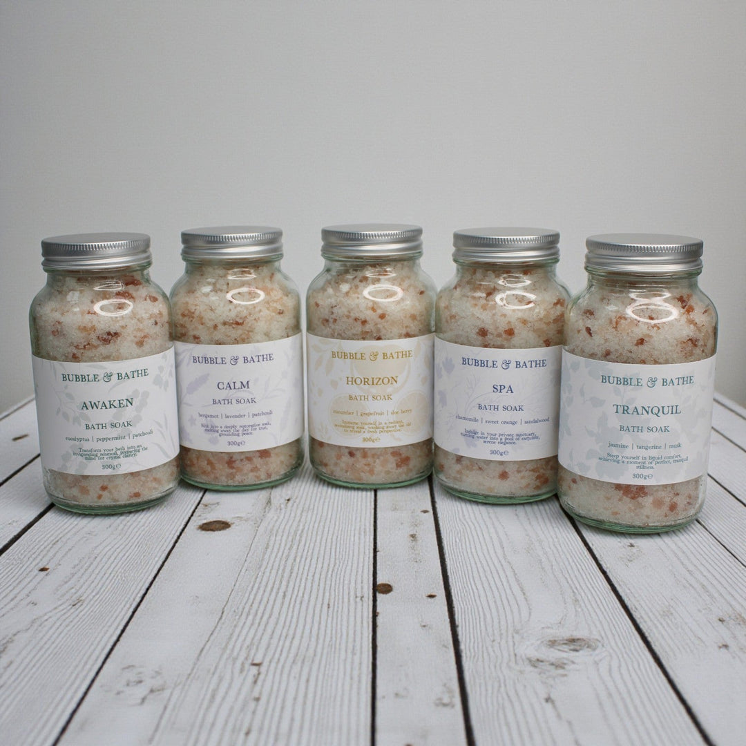 The full Bubble & Bathe Bath Soak collection, showing five jars of mineral bath salts in Awaken, Calm, Horizon, Spa, and Tranquil scents lined up on a white shelf.