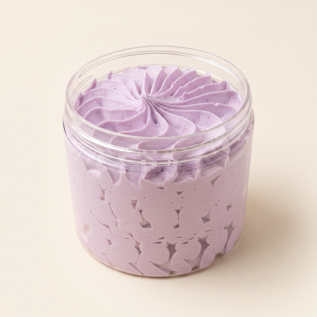 A clear cylindrical jar filled with light lavender whipped cream or body butter, topped with a piped swirled pattern. The jar is photographed on a clean, solid, warm off-white background.