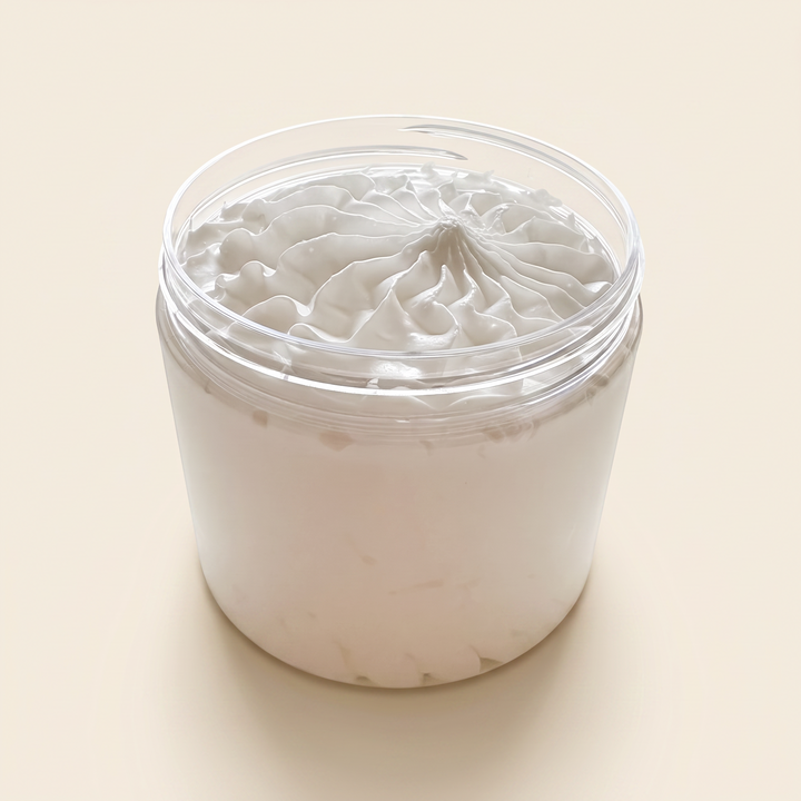 A clear cylindrical jar filled with thick, creamy off-white cosmetic or shaving product, topped with a matching clear lid and a textured white surface, shown on a plain warm beige background.